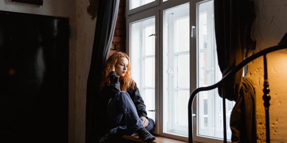 A woman looking sadly out a large window.